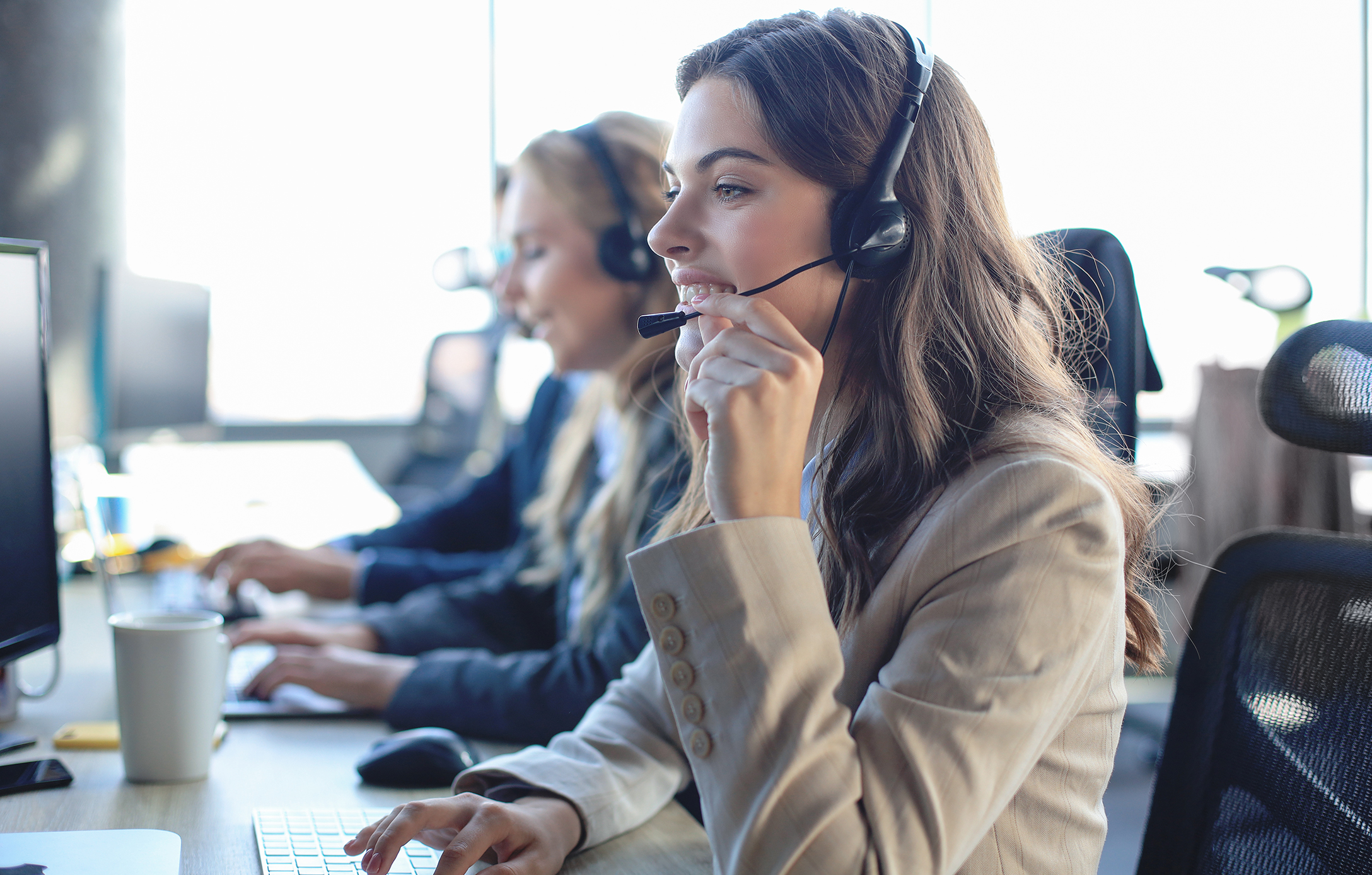 Female customer support operator with headset and smiling, with collegues at background